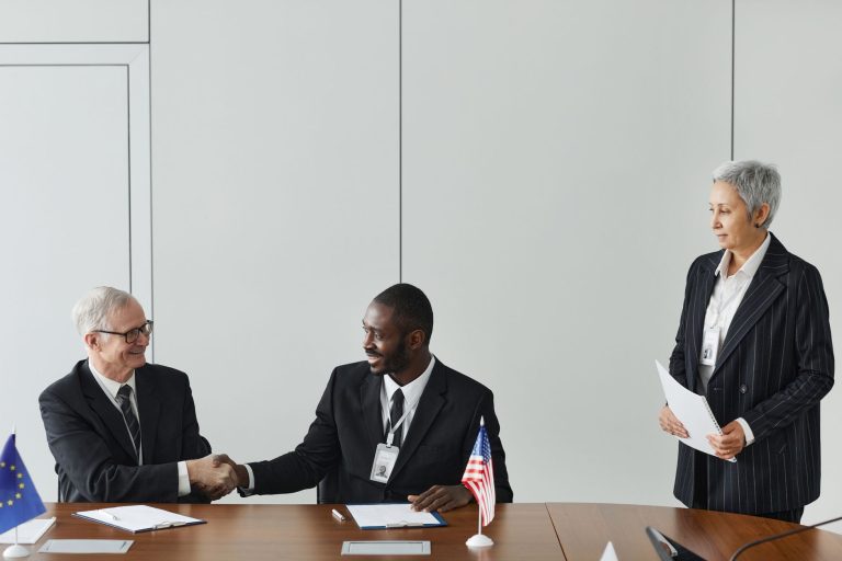Profissionais de diferentes países participam de uma reunião internacional e assinam um acordo em uma sala de conferências com bandeiras ao fundo.