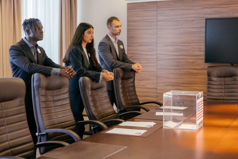 Grupo diverso de profissionais reunido em uma sala de conferências, discutindo ao redor de uma urna eleitoral.
