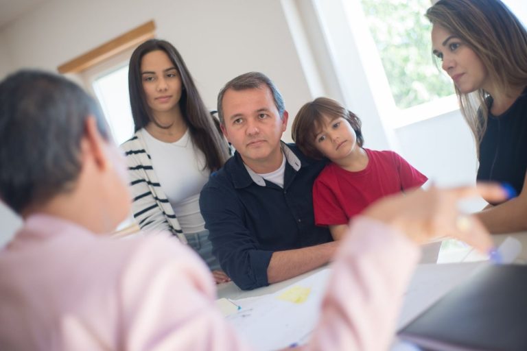 Família conversa com uma profissional durante um atendimento de orientação em uma sala iluminada.