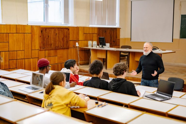 Estudantes participam de uma aula universitária com um professor em uma sala equipada com tecnologia.