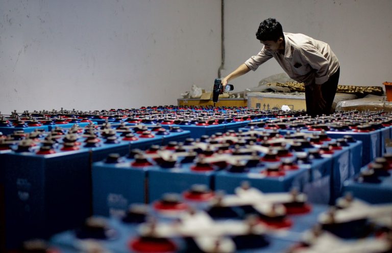 Trabalhador inspeciona fileiras de baterias industriais em uma instalação de armazenamento de energia.